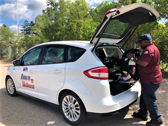 A Rides to Wellness operator in Flint, Michigan removes a carseat from the trunk in preparation for installing it to transport a child.