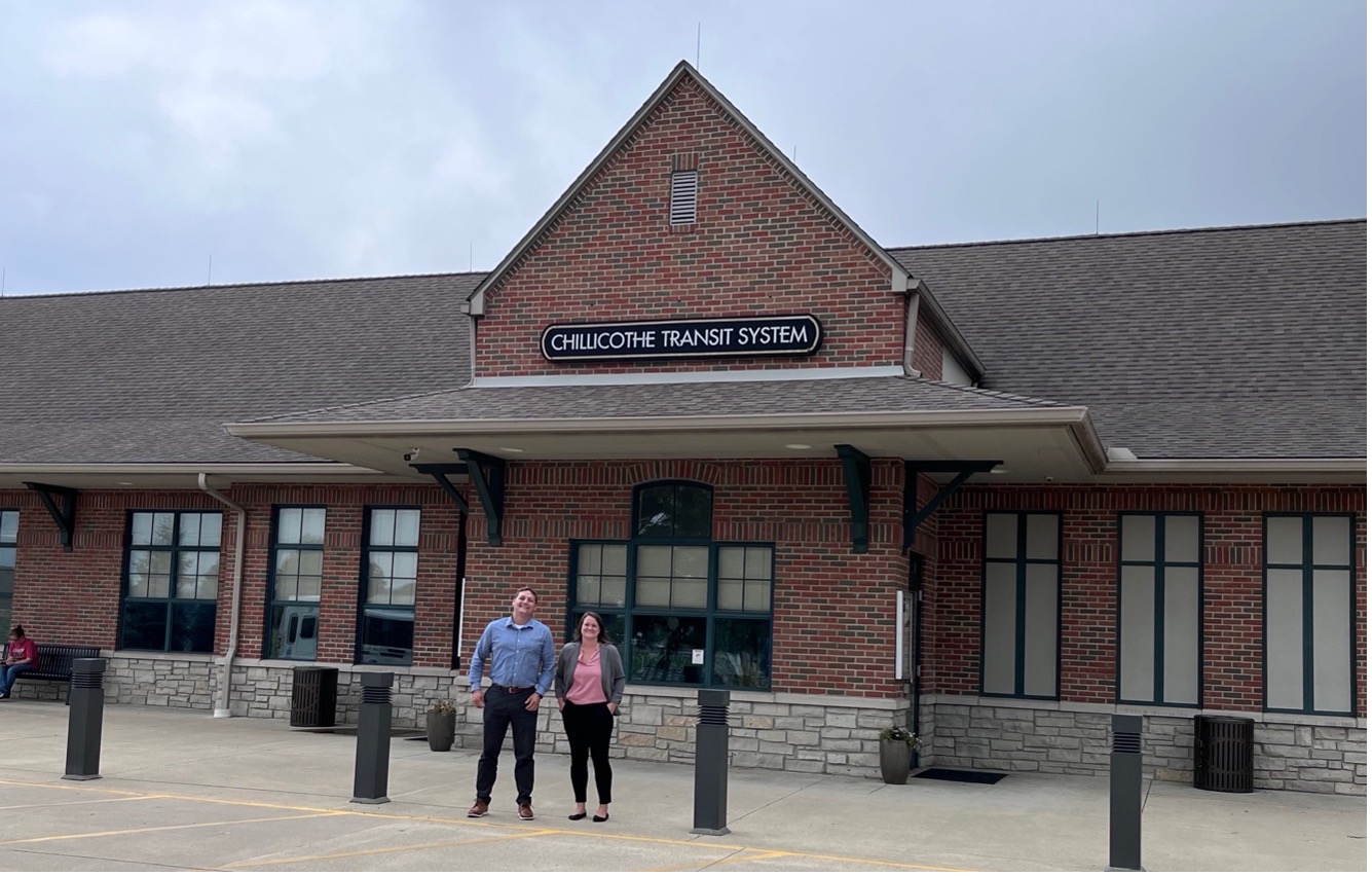 A white man and white woman stand in front of a large brick building with an A-frame, with Chillicothe Transit signage on front.