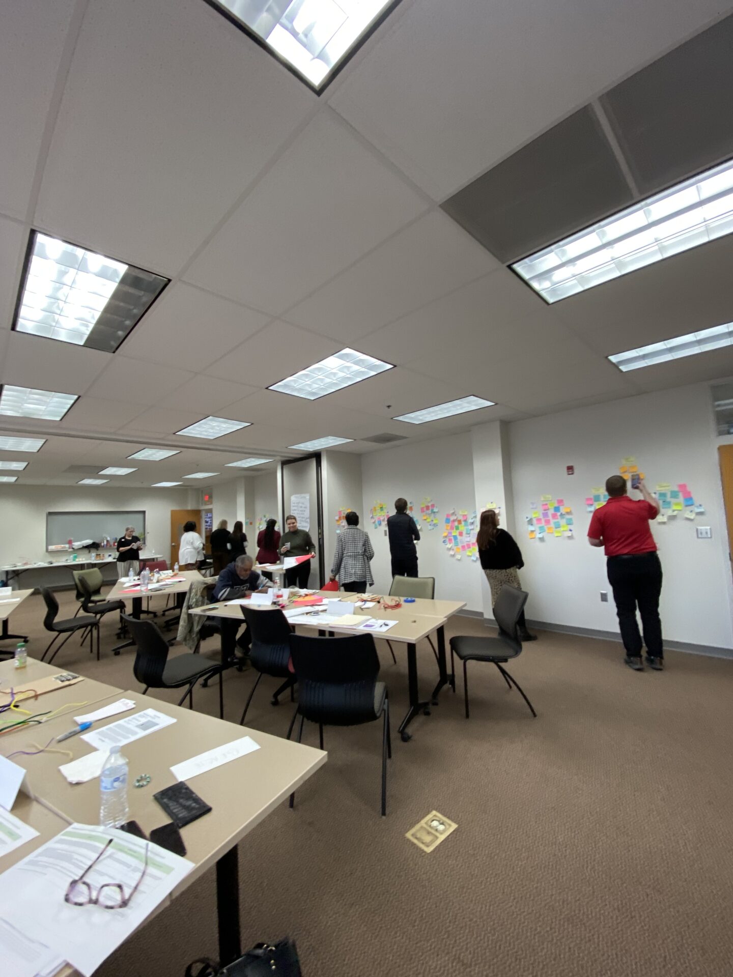 Arkansas workshop participants writing on small sticky notes on the front wall of the room.